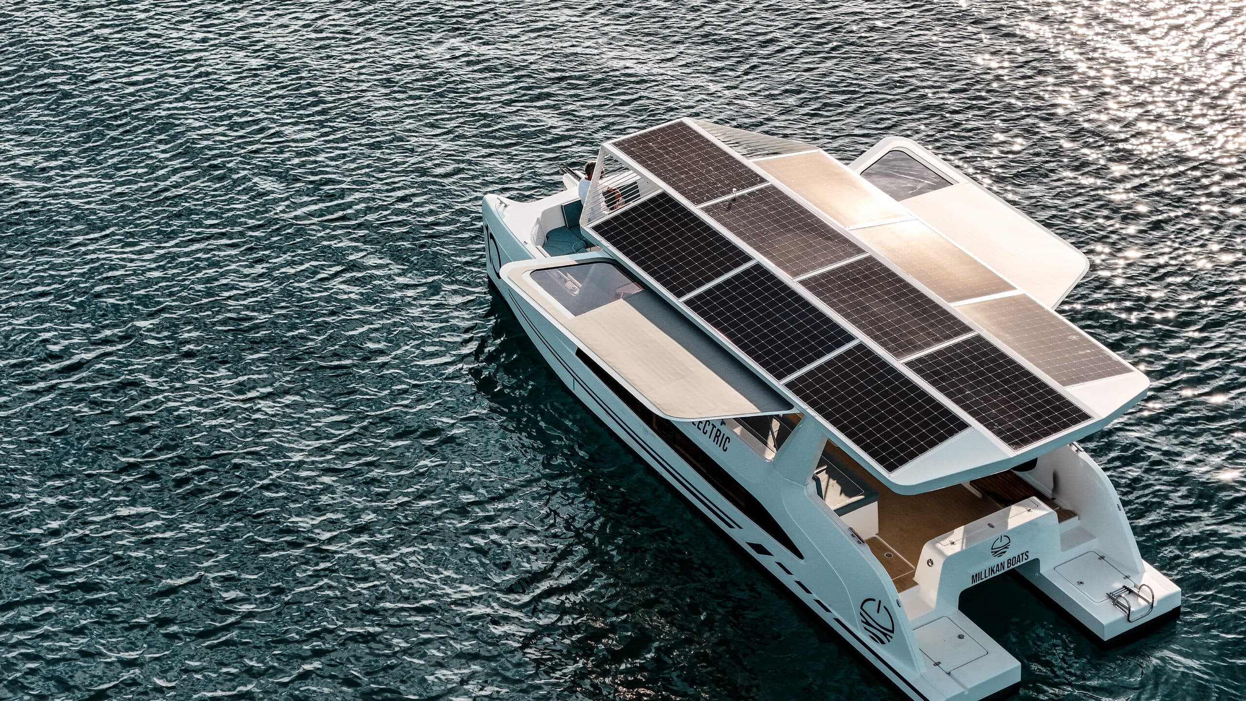Millikan M10 electric catamaran with a broad solar-panel canopy deployed while cruising on open water.