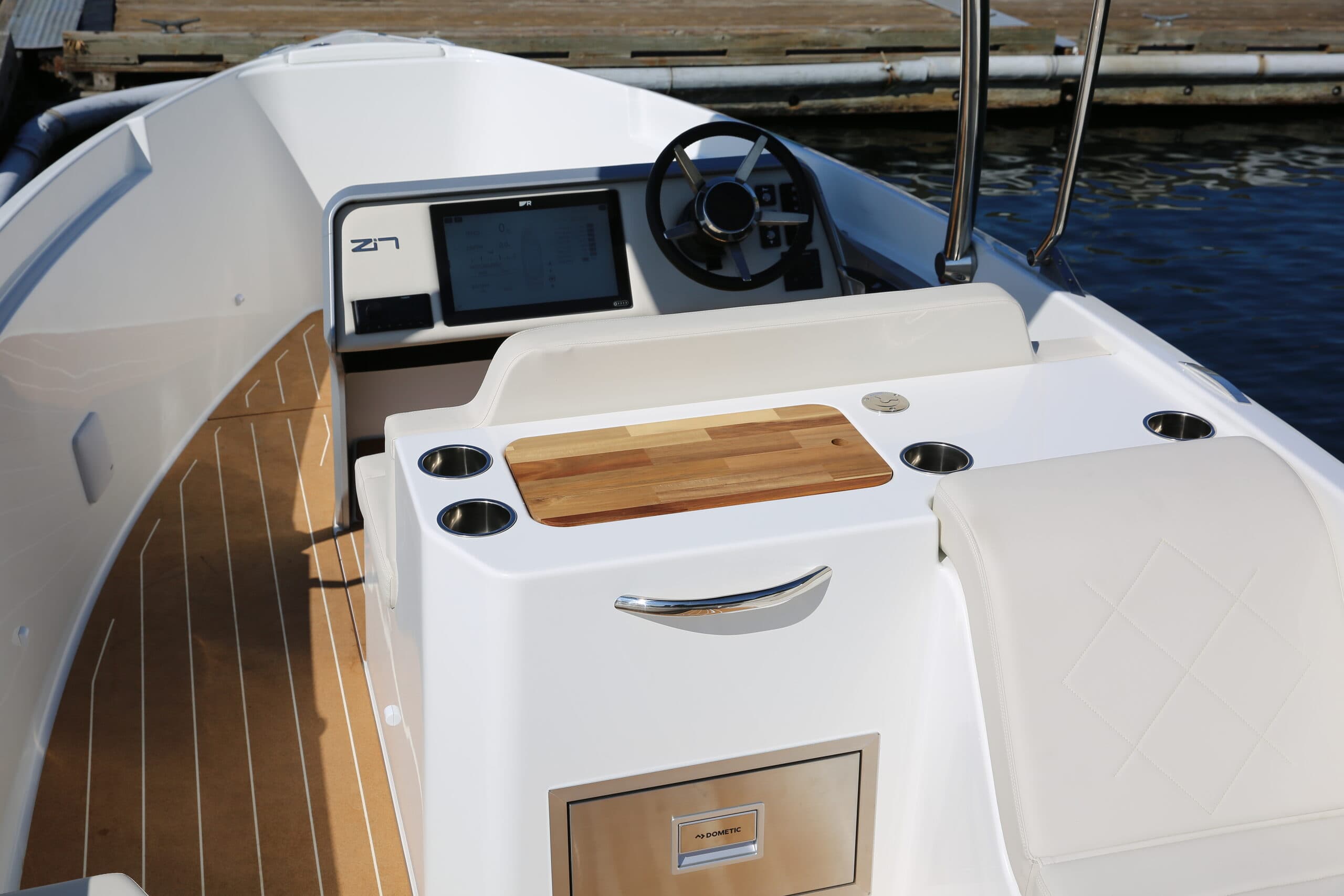 The helm of an electric boat featuring a clean, modern layout with integrated controls, a multifunction display, wraparound seating, and a built-in prep station with cup holders and a cutting board.
