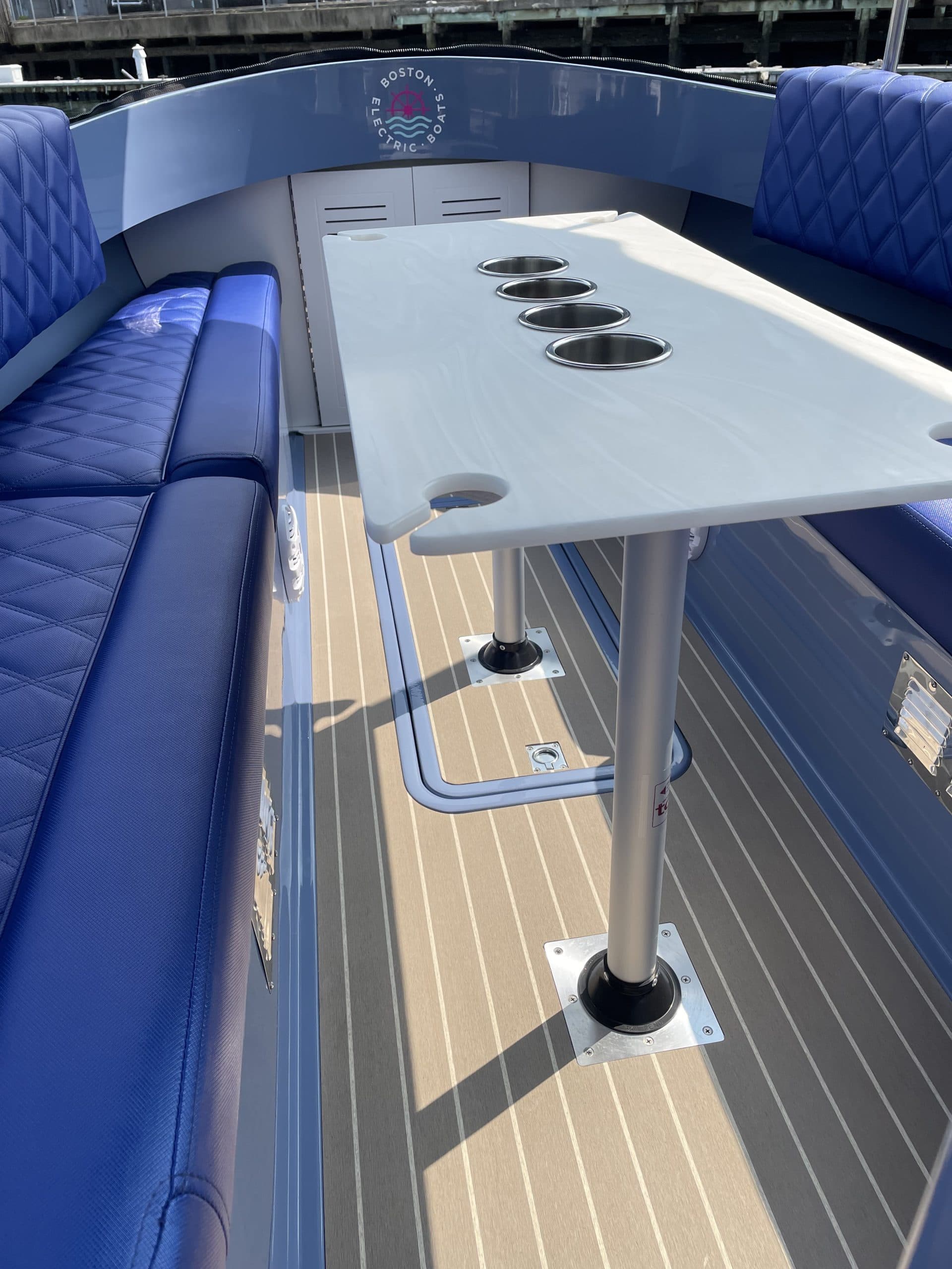 Interior of a Vision Marine Fantail 217 with blue quilted seating, a central table with cupholders, and striped deck flooring.