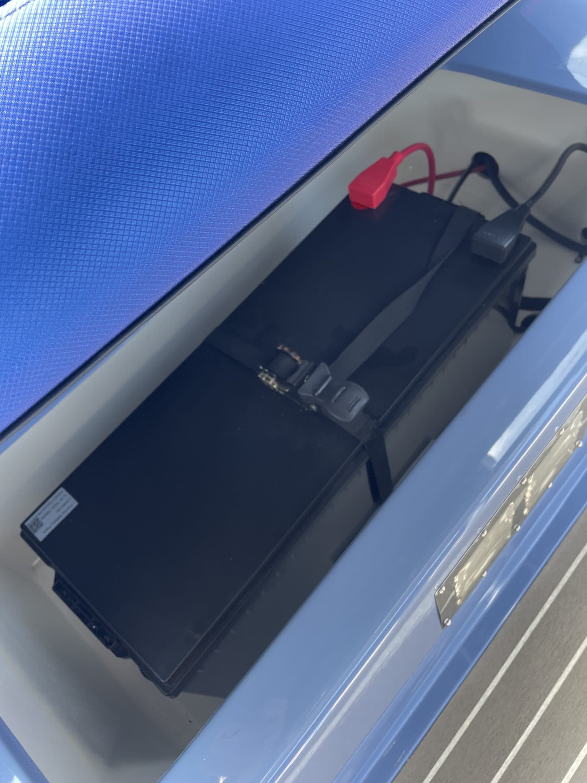 Vision Marine Fantail 217 Battery compartment with a black battery pack, red and black cables, and securing straps inside a blue electric boat.