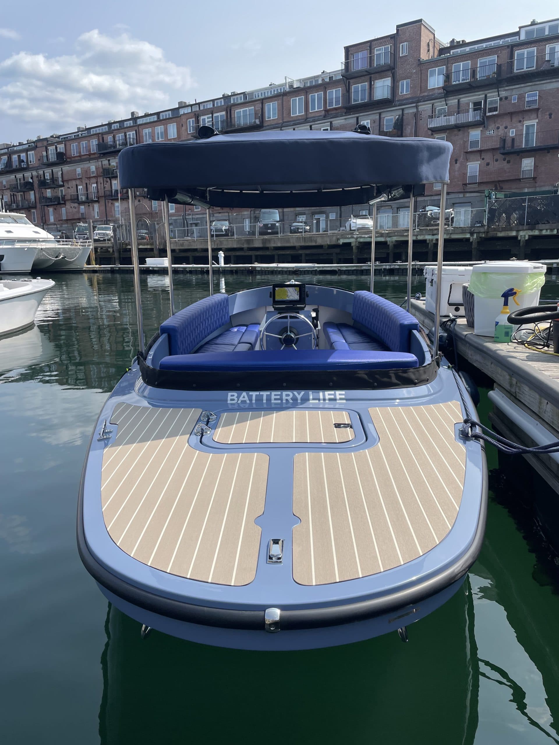 Vision Marine Fantail 217 electric boat docked in a marina, viewed from the stern with canopy raised and “Battery Life” branding visible.