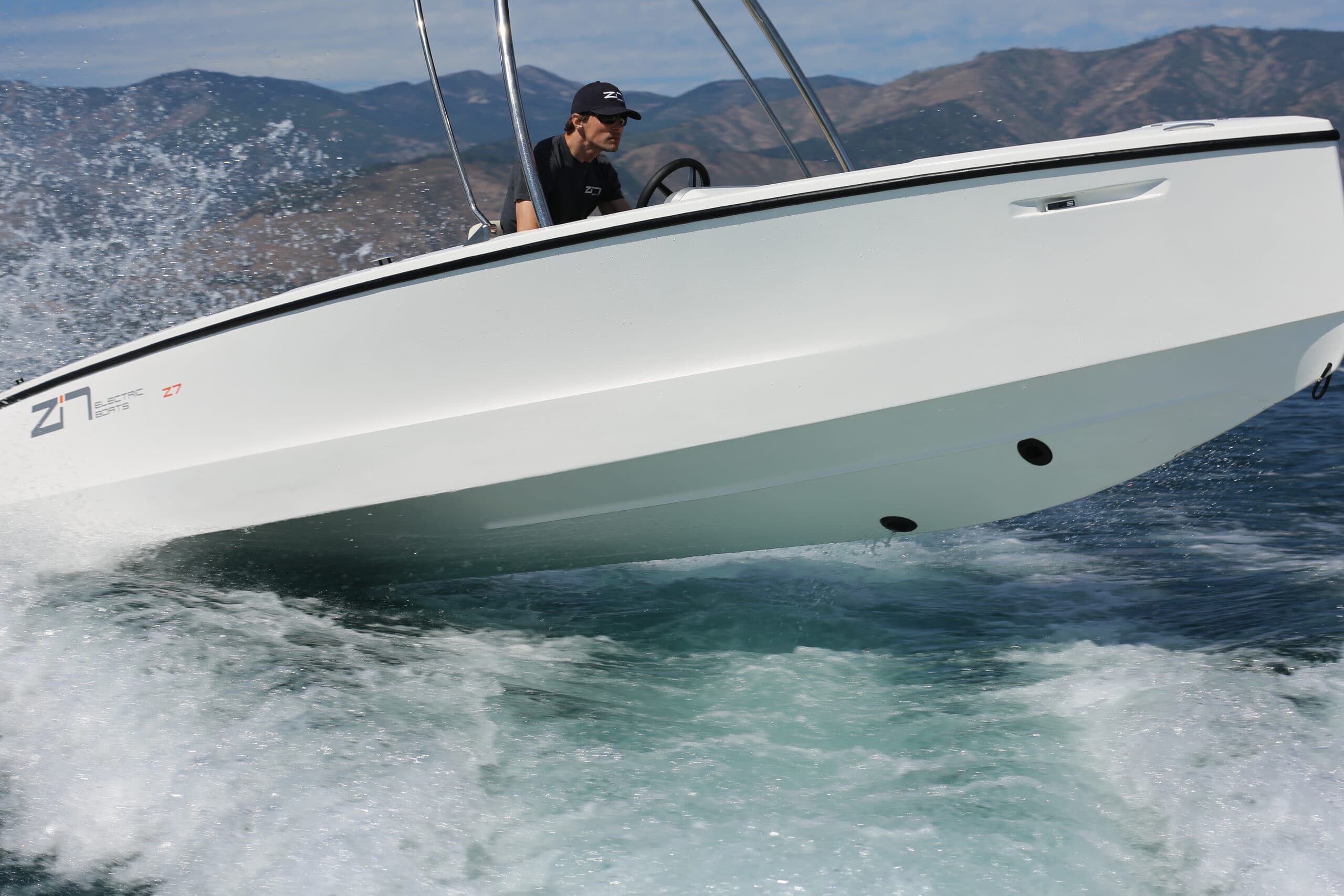White Zin Boats Z7 motorboat speeding across choppy water, with a driver at the helm and mountainous coastline in the background.