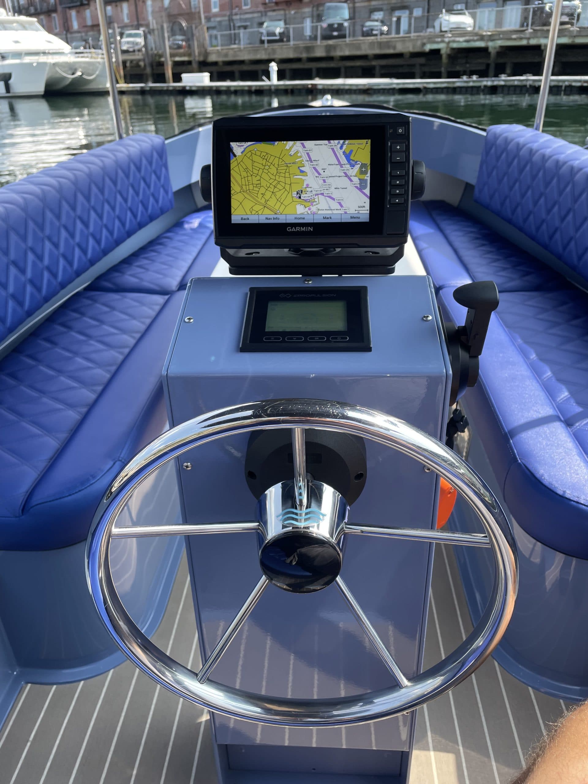 Helm of a blue electric Vision Marine Fantail 217 with a navigation display, chrome steering wheel, control panel, and quilted seating.