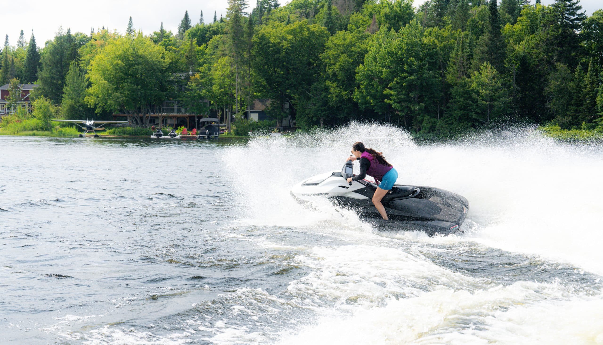 Taiga Orca P2 speeding across a lake, viewed from the side, with a rider creating a broad spray.