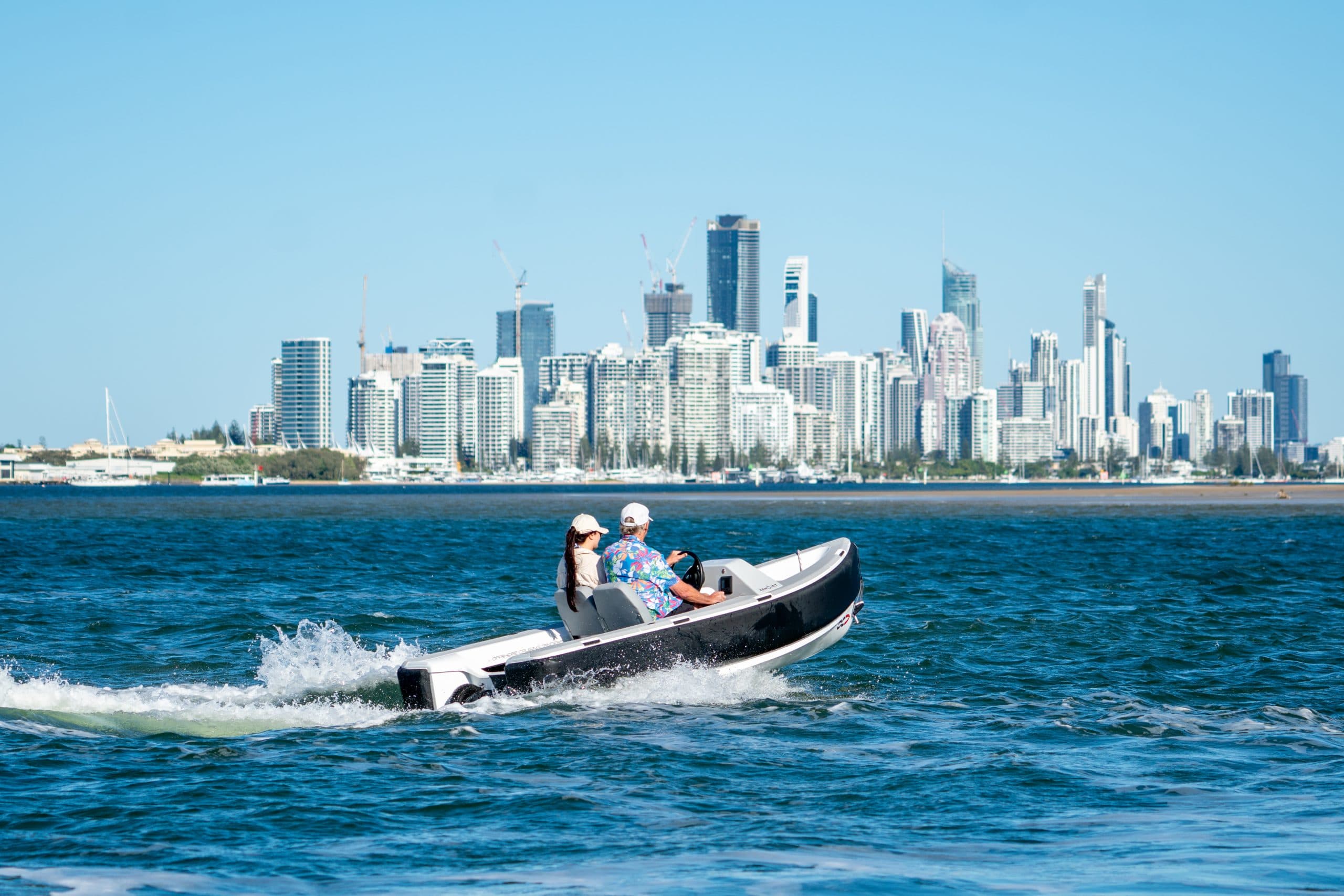Side view of a 2026 Offshore Cruising Tenders OC330 cruising across the water, with a city skyline in the background.