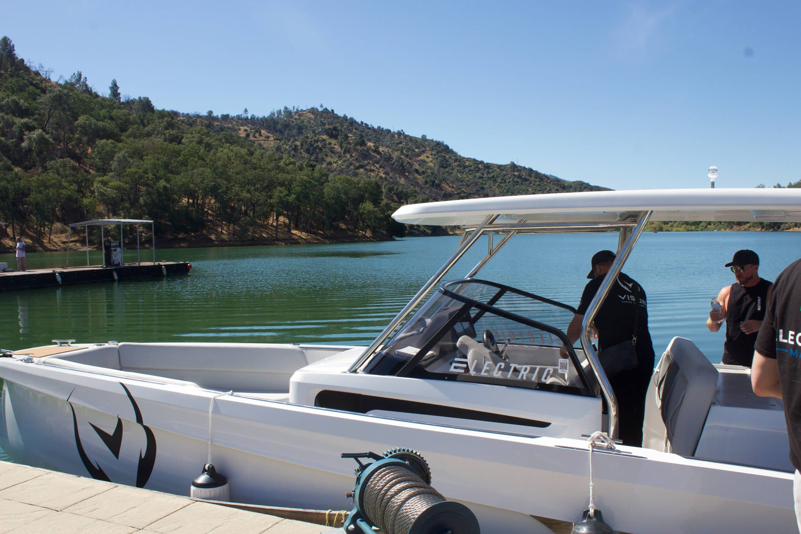 Sterk 31E viewed from the side, showing the open cockpit, windshield, canopy, and people aboard at a lakeside dock