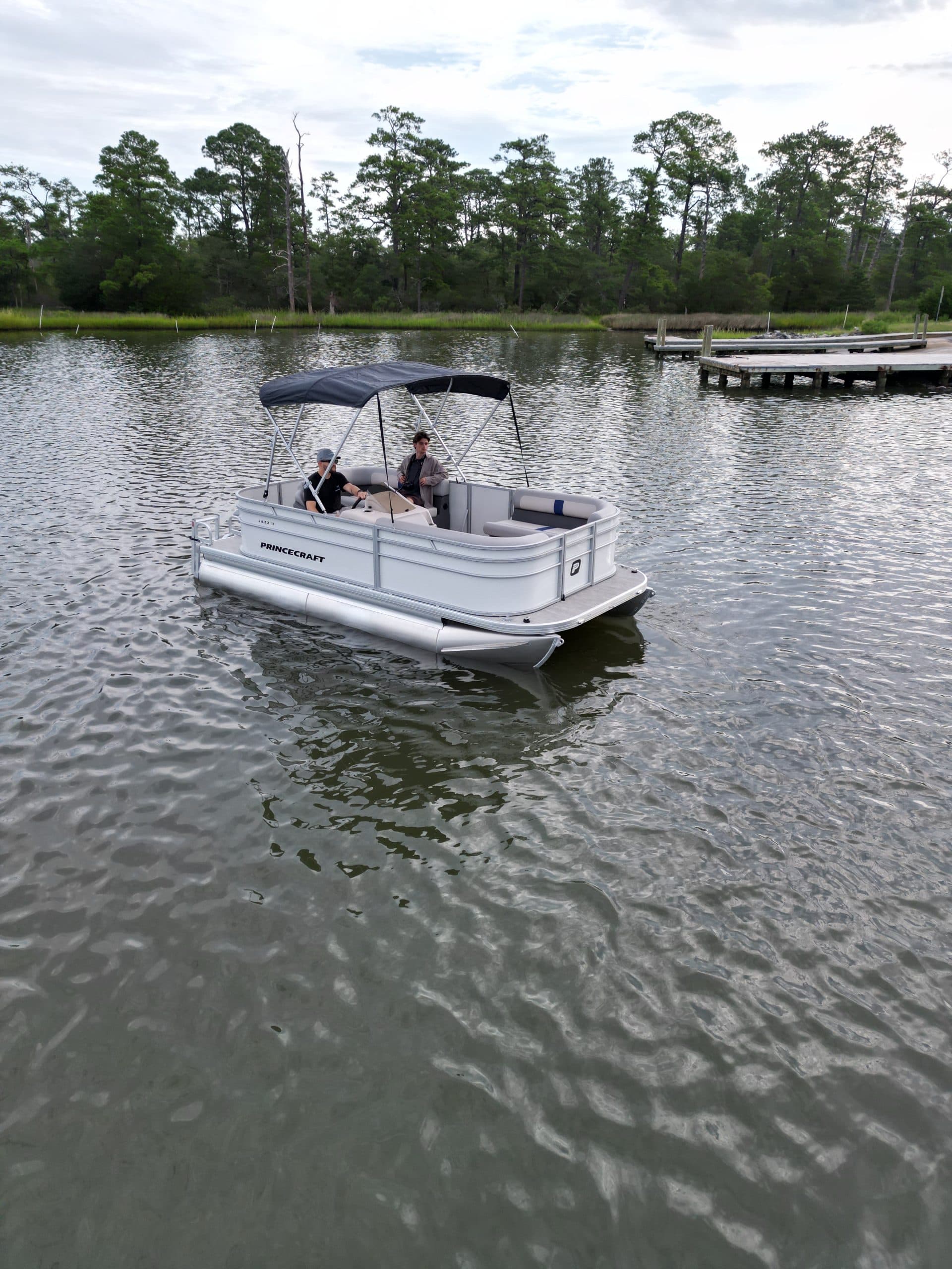 Princecraft Jazz 17 pontoon boat viewed from the side on a lake, with a canopy and seating visible.