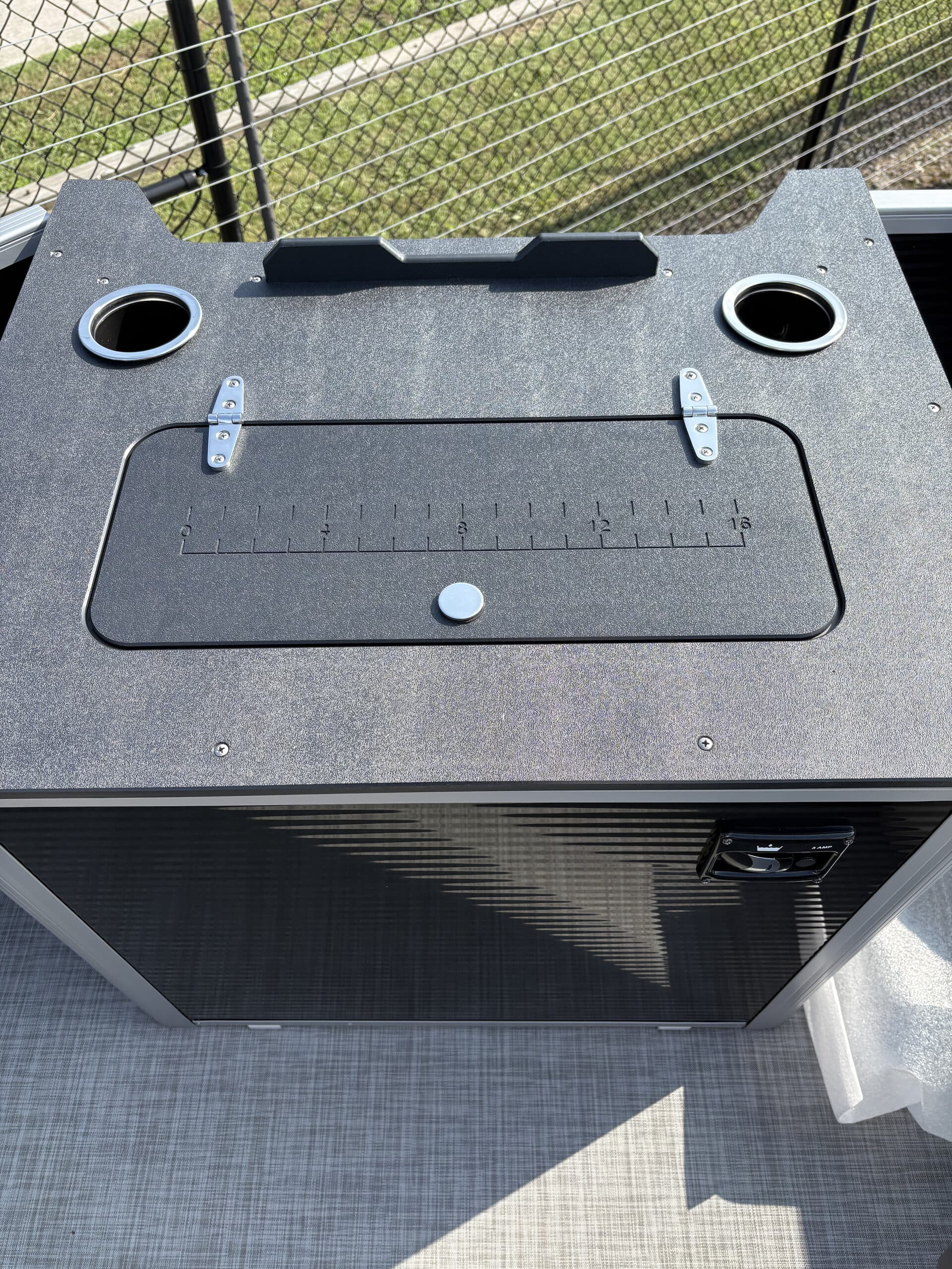 Close view from above of a black storage hatch with two cup holders on a boat (2026 Princecraft Jazz 19 4s) deck