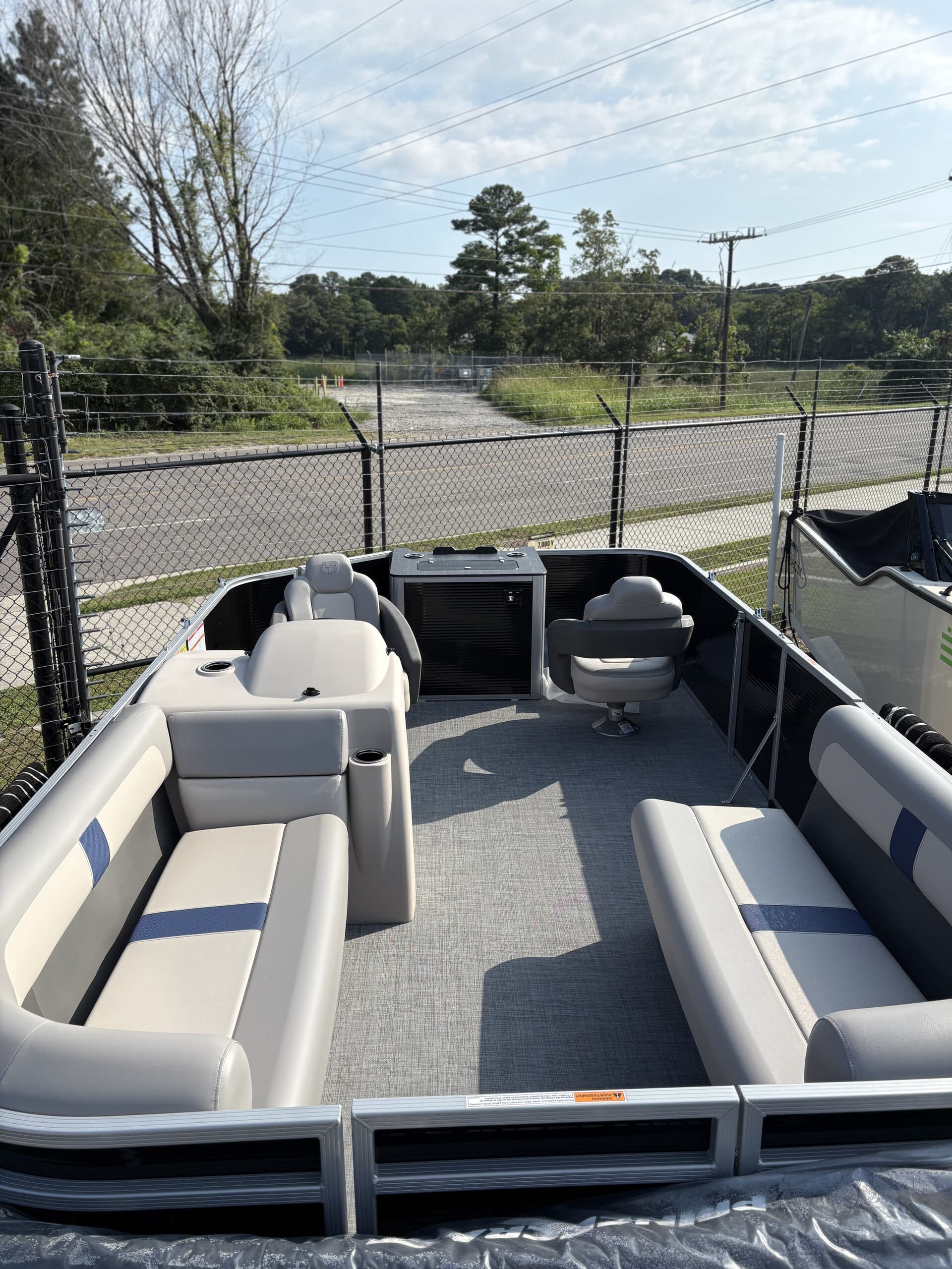 View from the stern into the cockpit of a pontoon boat (2026 Princecraft Jazz 19 4s), showing cushioned seating on sides, helm console, and open center walkway.