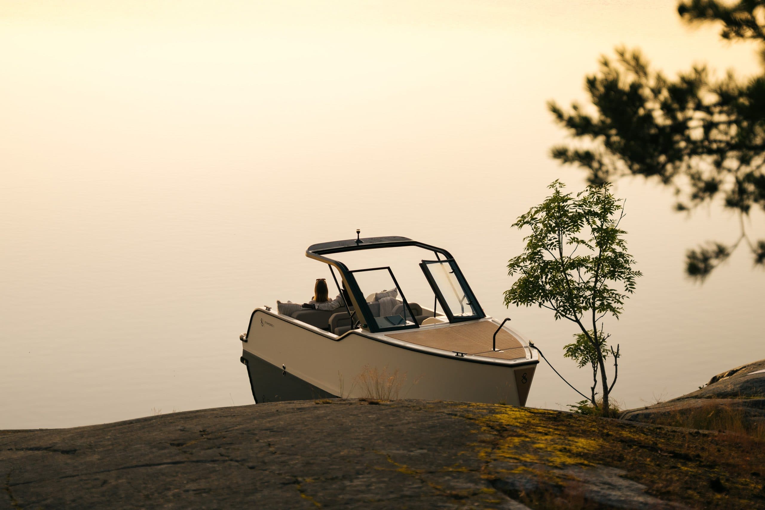 X Shore XS1 viewed from shore at sunset, showing the boat’s exterior, bow, windshield, and open cockpit.