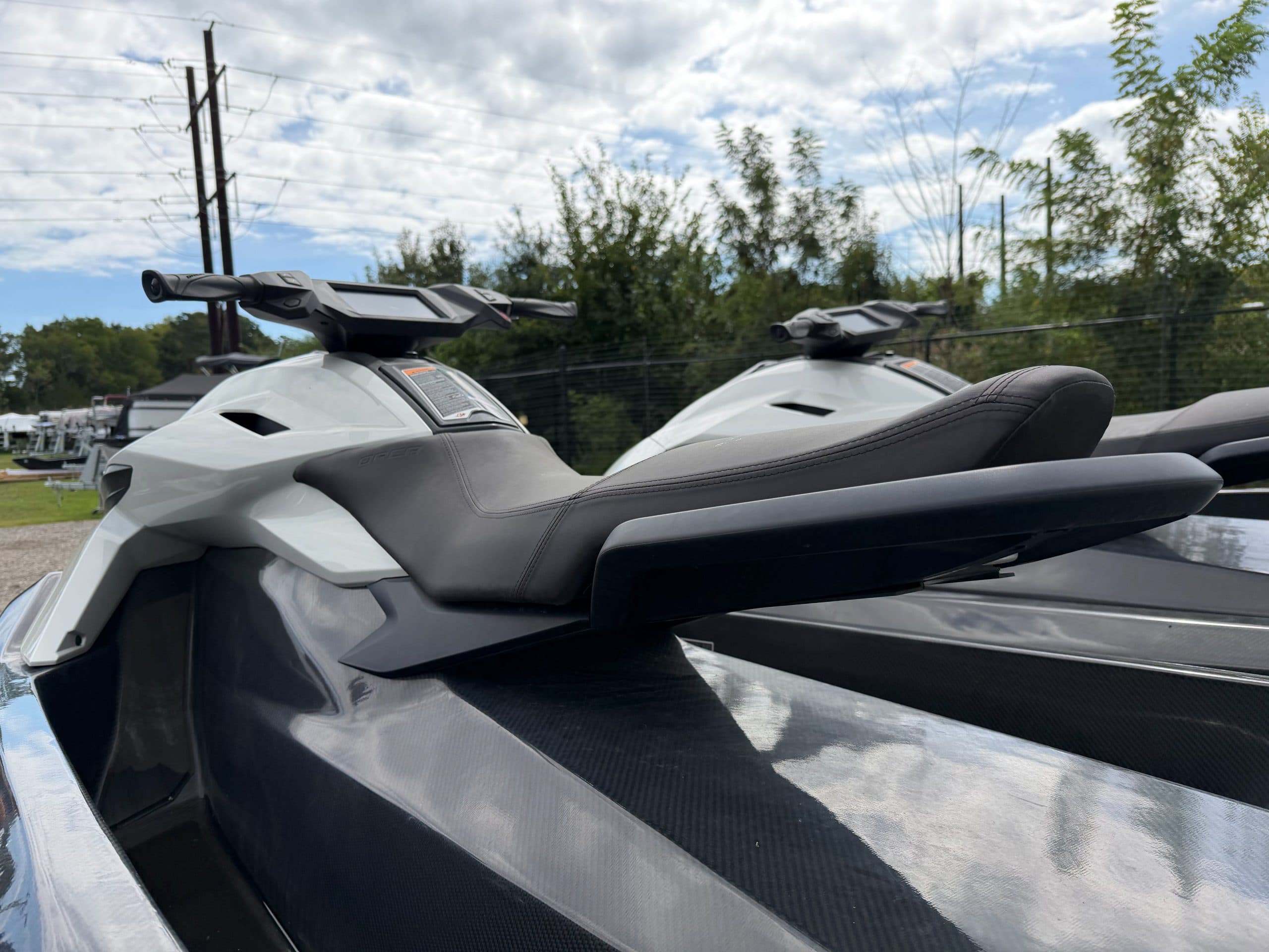 Close-up side view of two personal watercraft, showing their angular hulls, seats, handlebars, and carbon-fiber deck surfaces.
