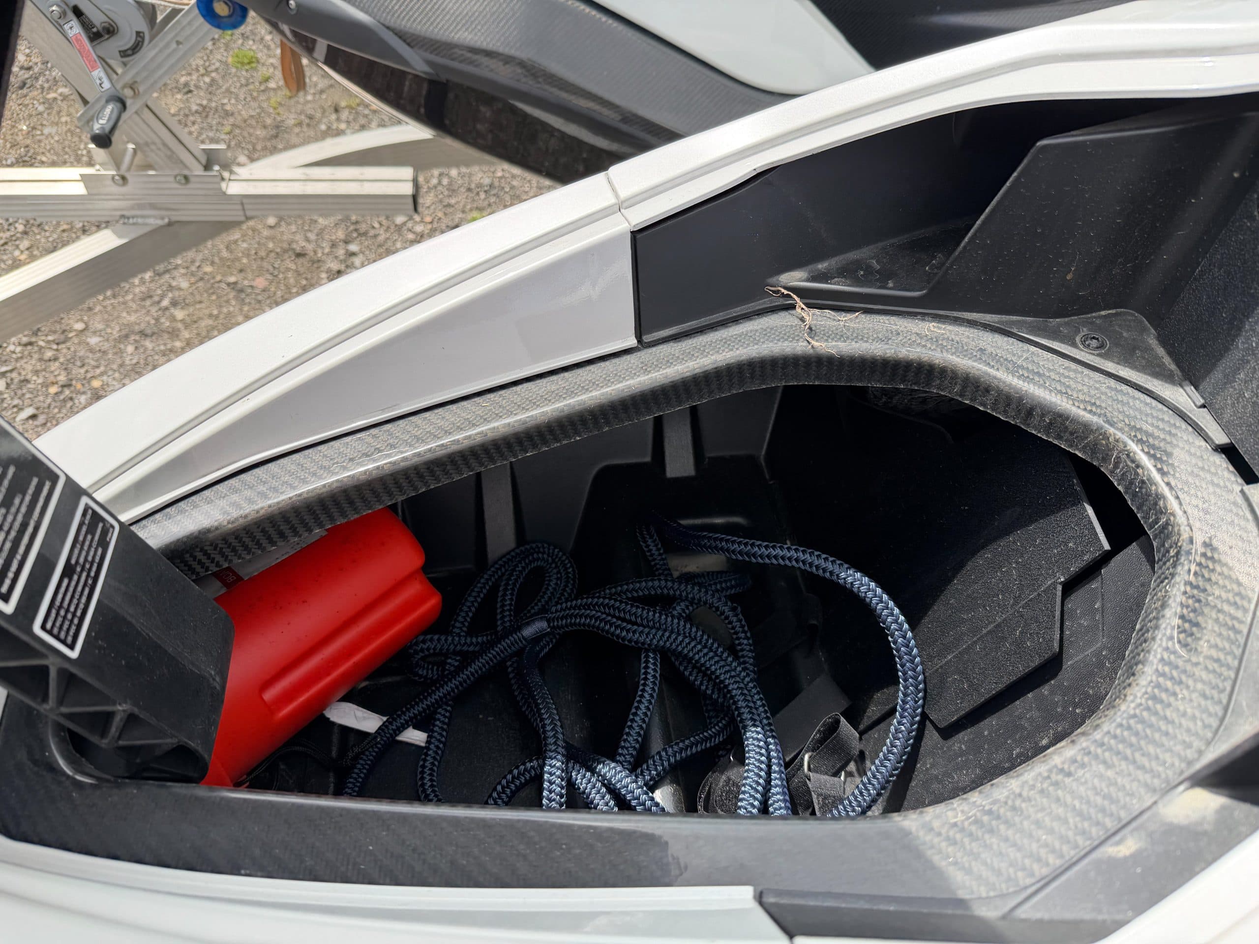 Open bow storage compartment of a carbon-fiber personal watercraft Taiga Orca, viewed from above, with coiled rope and red safety equipment inside.