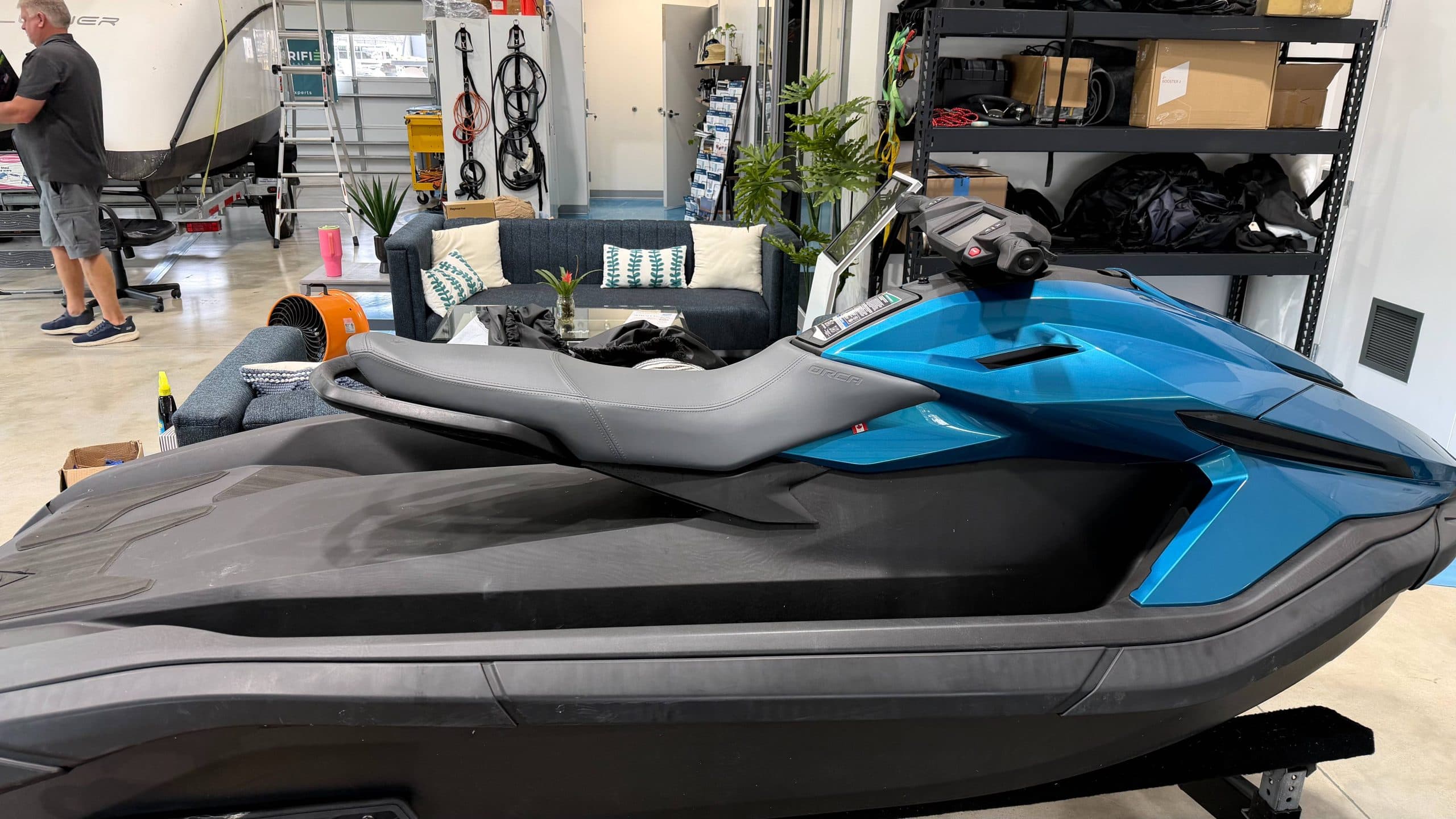 Side view of a Taiga Orca P2 personal watercraft displayed indoors, showing its black-and-blue hull, seat, handlebars, and front bodywork.