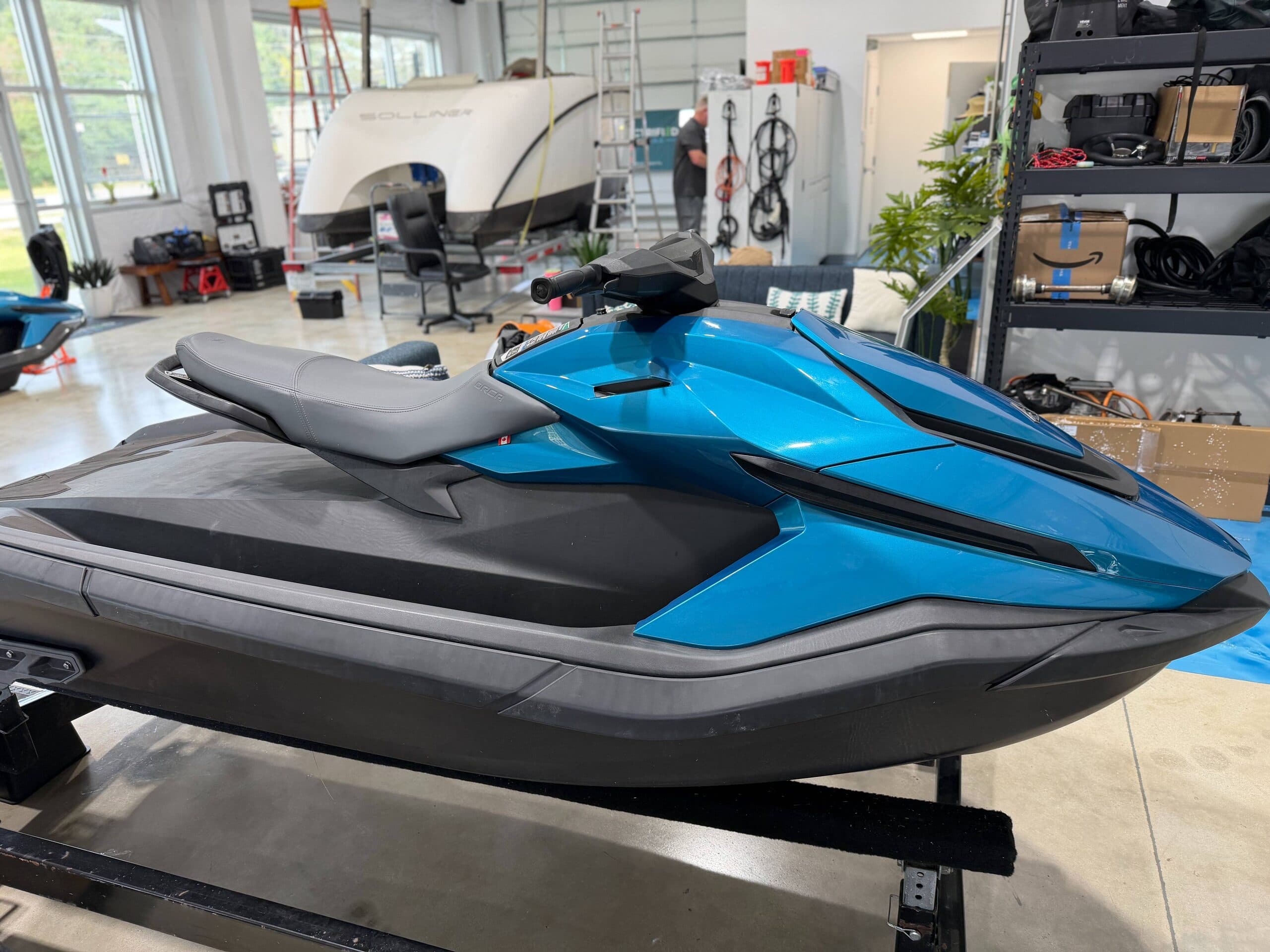 Side view of a blue and black personal watercraft (Taiga Orca P2) on a trailer, showing the seat, handlebars, and pointed bow indoors.
