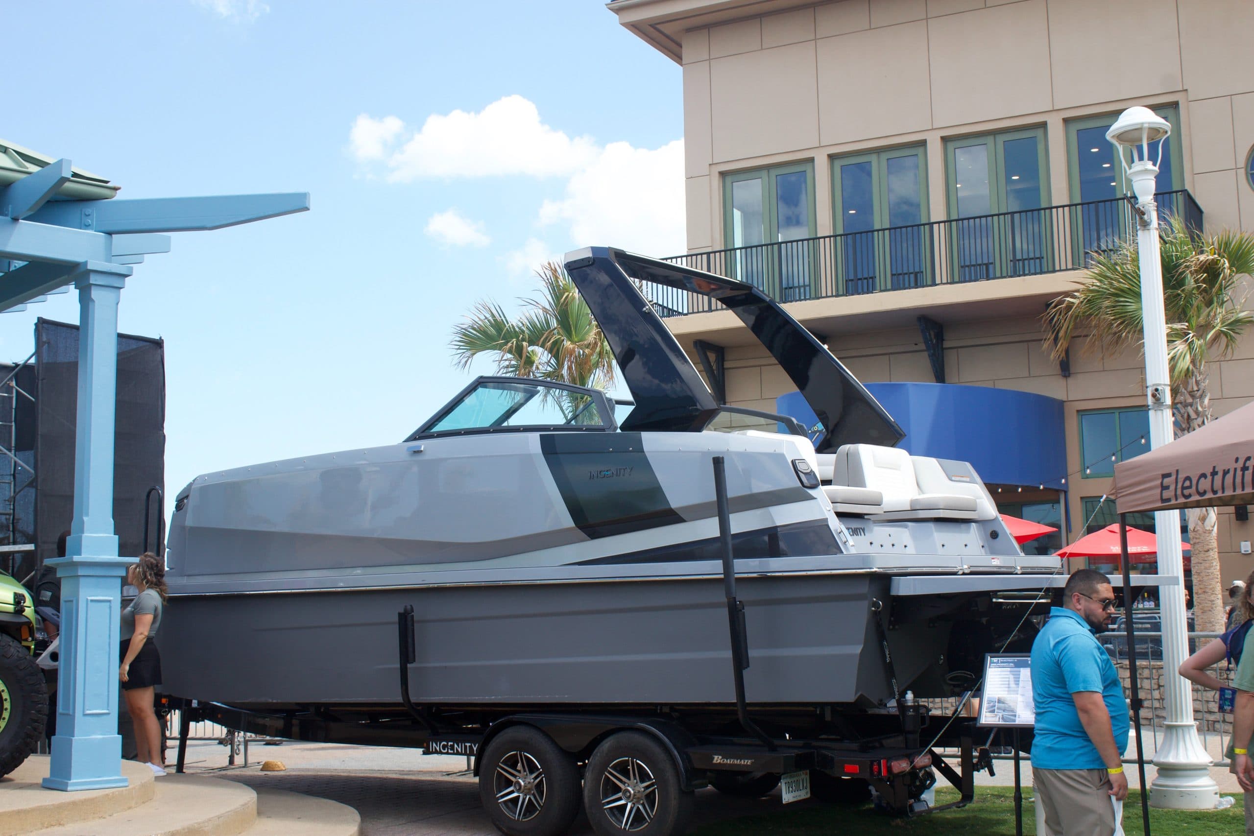 Side view of a modern motorboat on a trailer, showing the hull, windshield, open cockpit, and raised canopy.