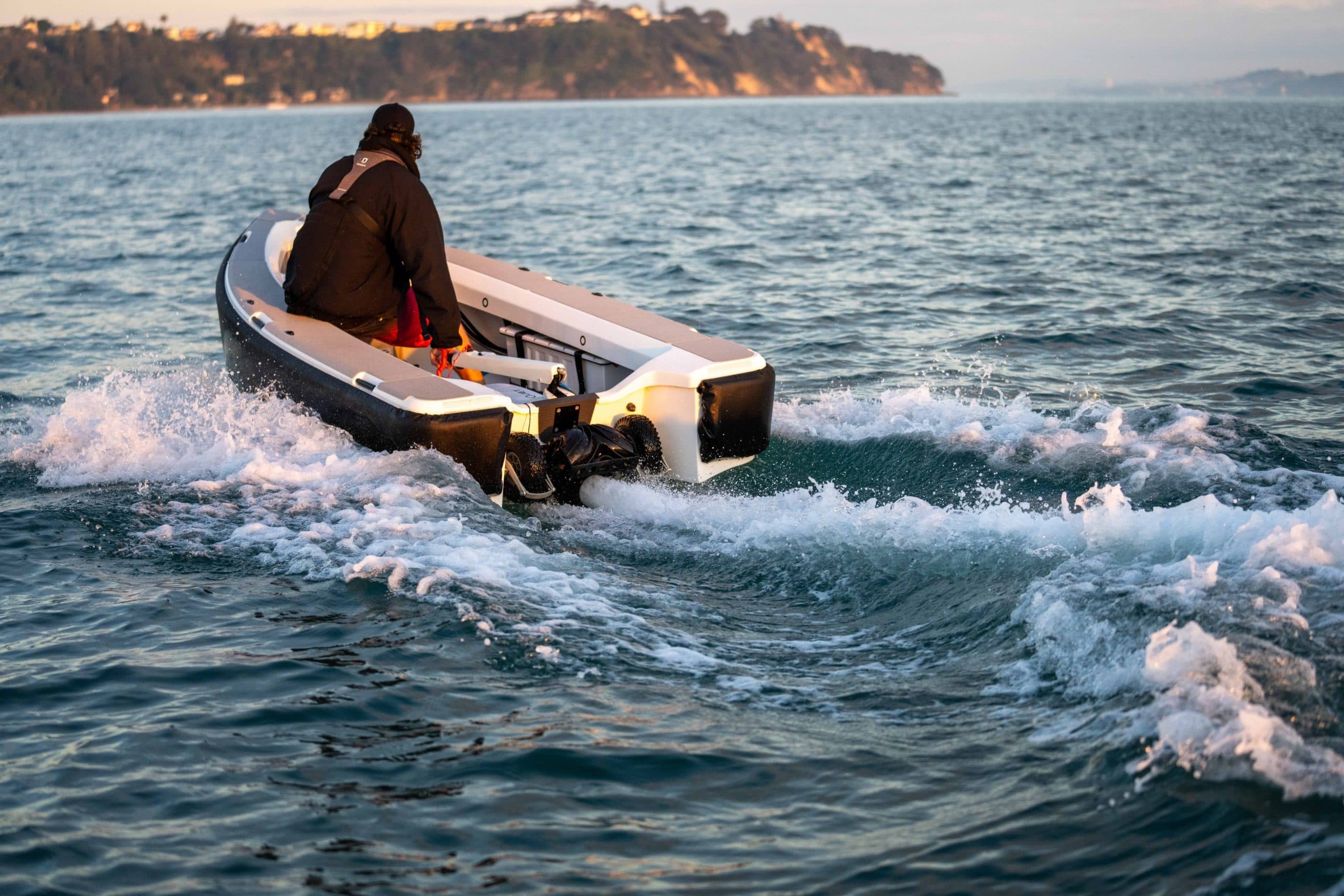Rear view of a 2026 Offshore Cruising Tenders OC350 underway, with an outboard motor and a person seated near the stern.