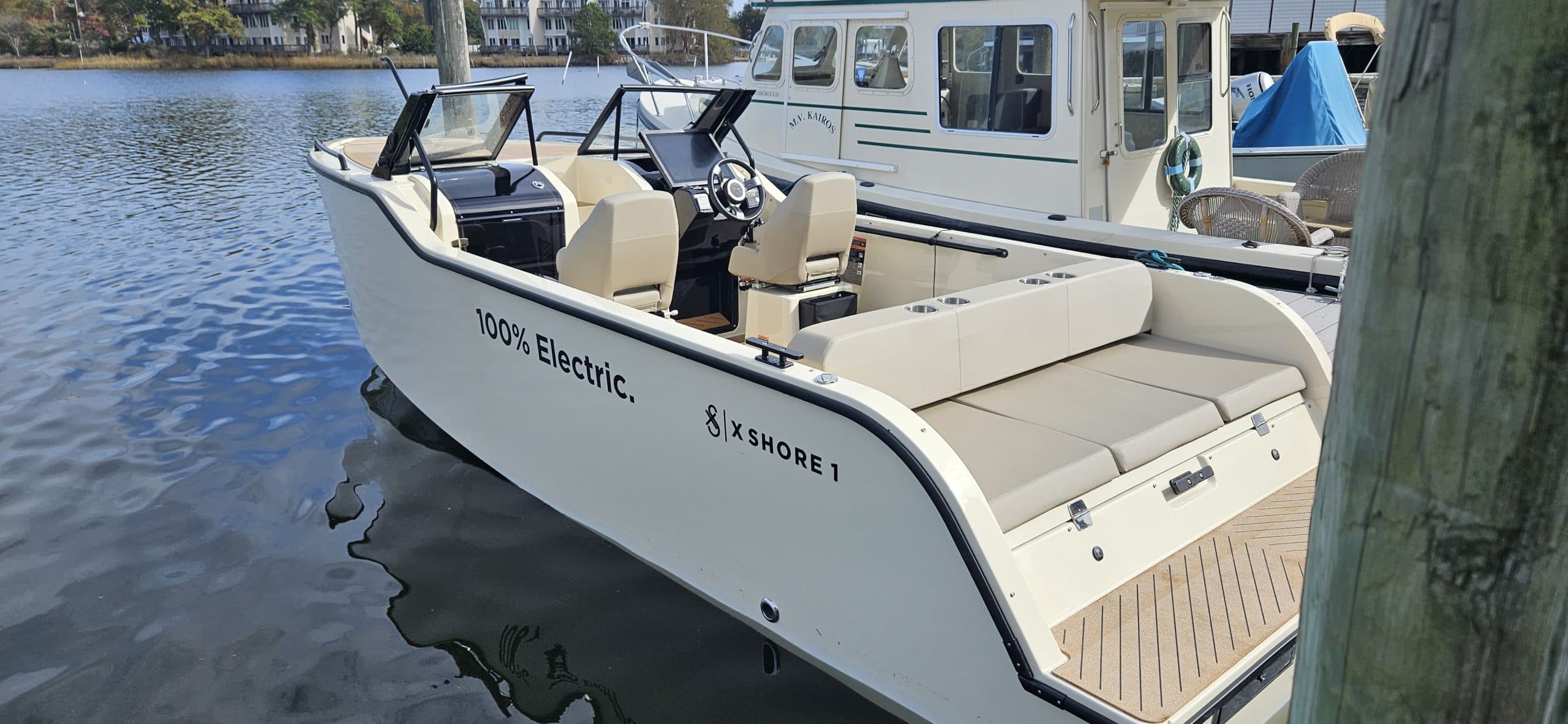 X Shore 1 electric boat viewed from the side at the dock, showing the bow seating area, open cockpit, and stern swim platform.