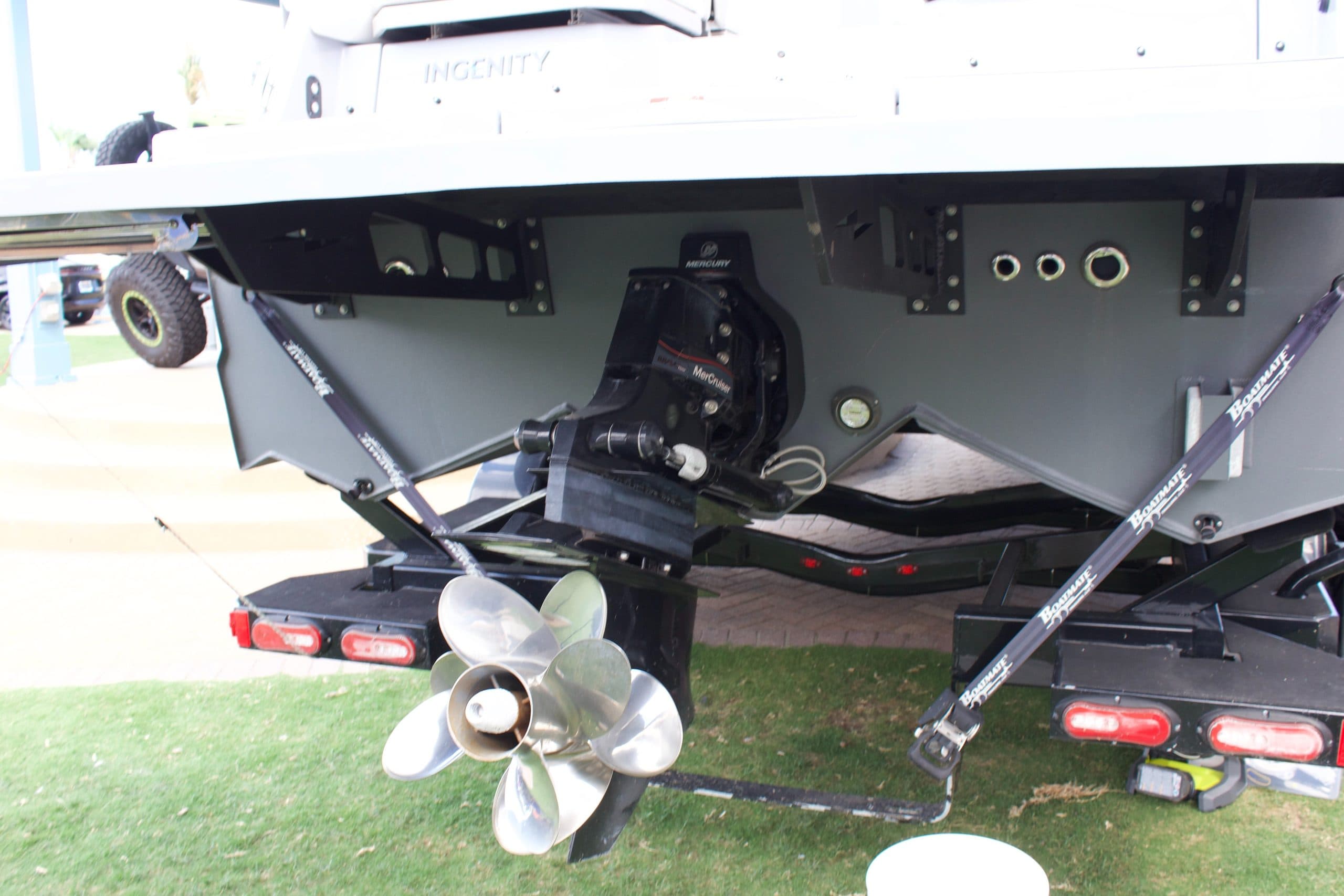 Rear view of a boat showing the exposed propulsion unit, propeller, trim hardware, trailer, and underside of the hull.