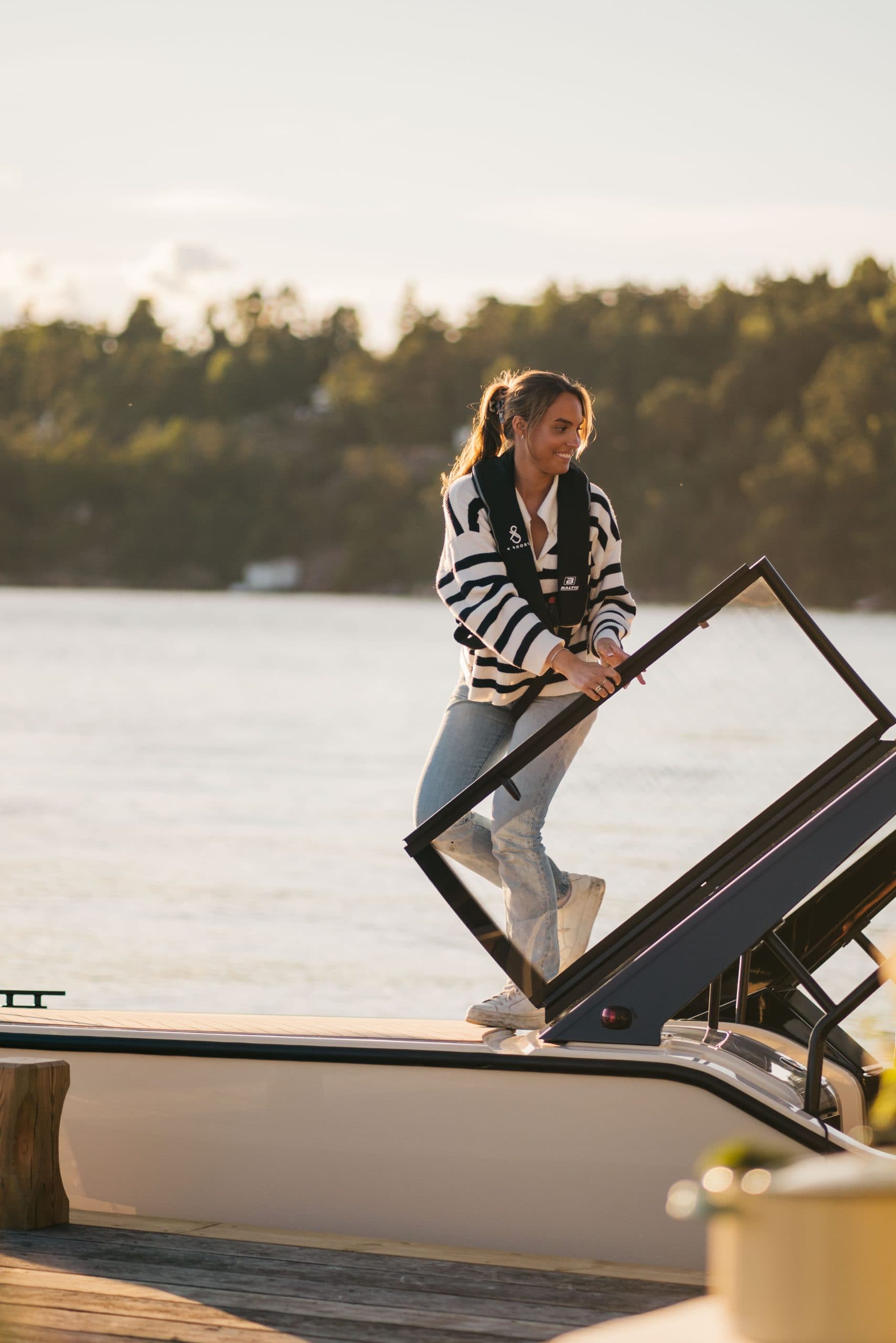 Person standing on the side deck of the X Shore XS1, holding a railing, viewed from the dock.
