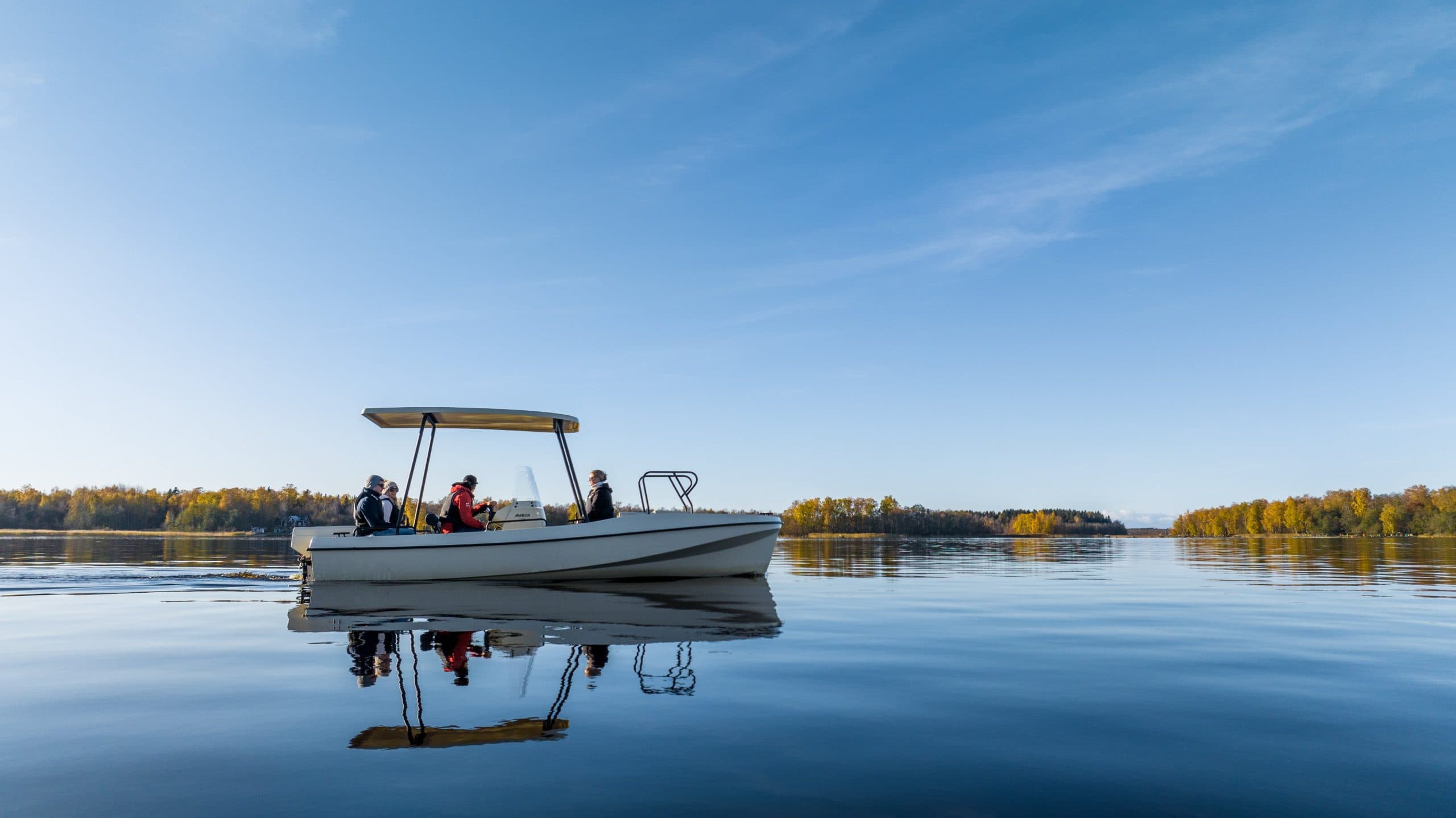Elvene Amber on calm water, viewed from the side with people aboard and a canopy raised.