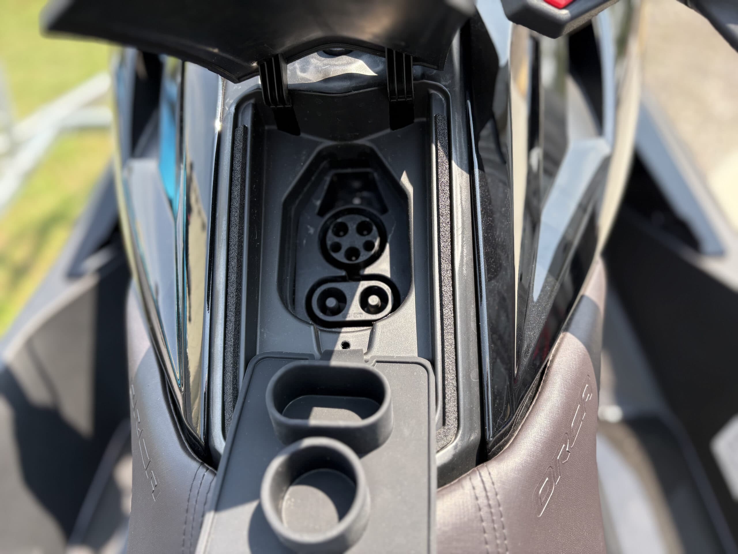 Close-up, top-down view of a watercraft (2026 Taiga Orca P2) console compartment with a circular connector, two cup holders, and surrounding trim.