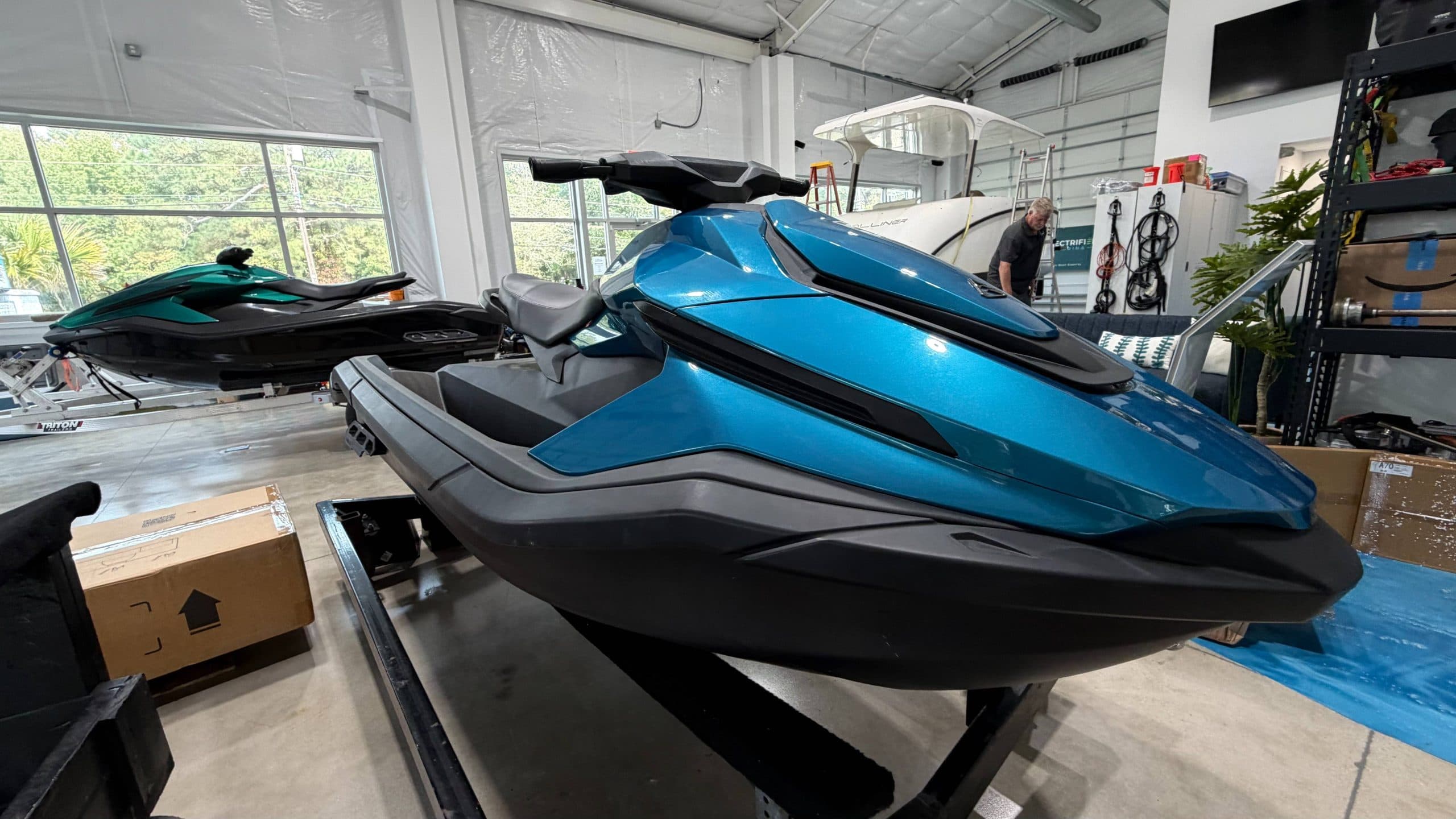 Side-front view of a blue personal watercraft (Taiga Orca P2) on a display stand in a workshop.