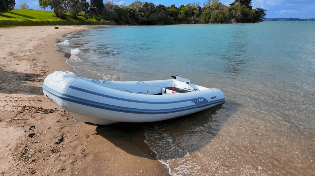 AB T11 inflatable boat resting at the edge of a sandy beach, viewed from shore at an angle.