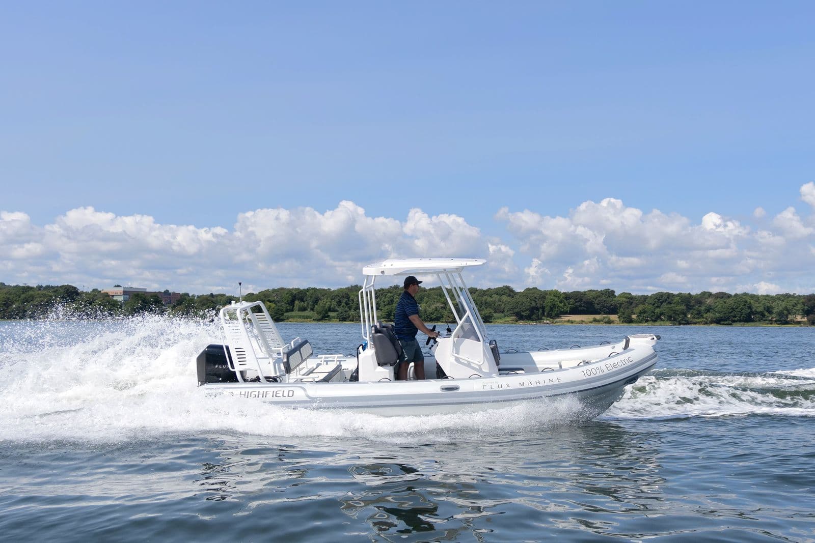 Highfield Sport 660 rigid inflatable boat speeding across a lake, creating a broad wake under a sunny sky.