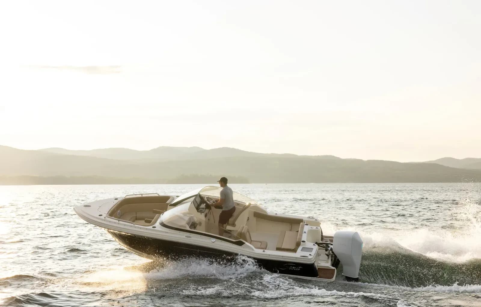 Scout 215 Dorado cruising on open water, viewed from the side with a person at the helm and hills in the background