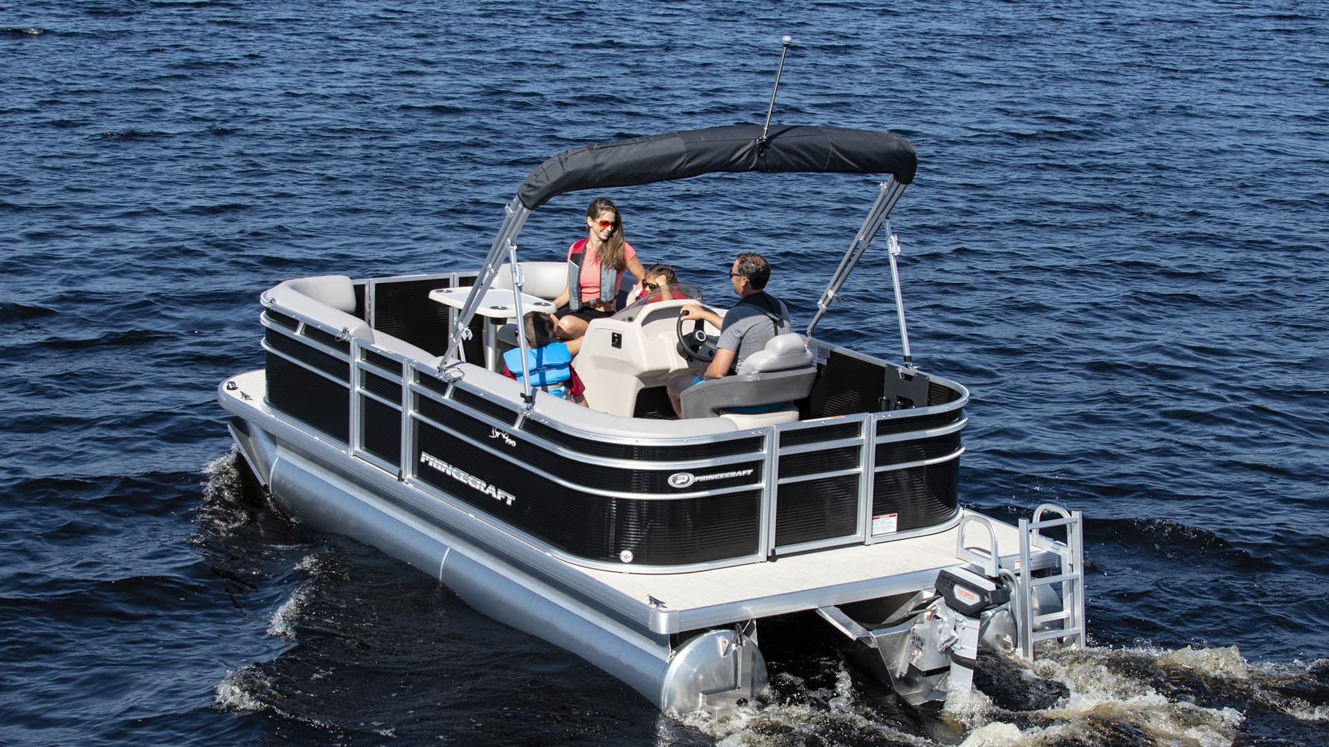 Princecraft Brio E17 pontoon boat cruising on open water with a black canopy, two visible passengers, and an outboard motor.