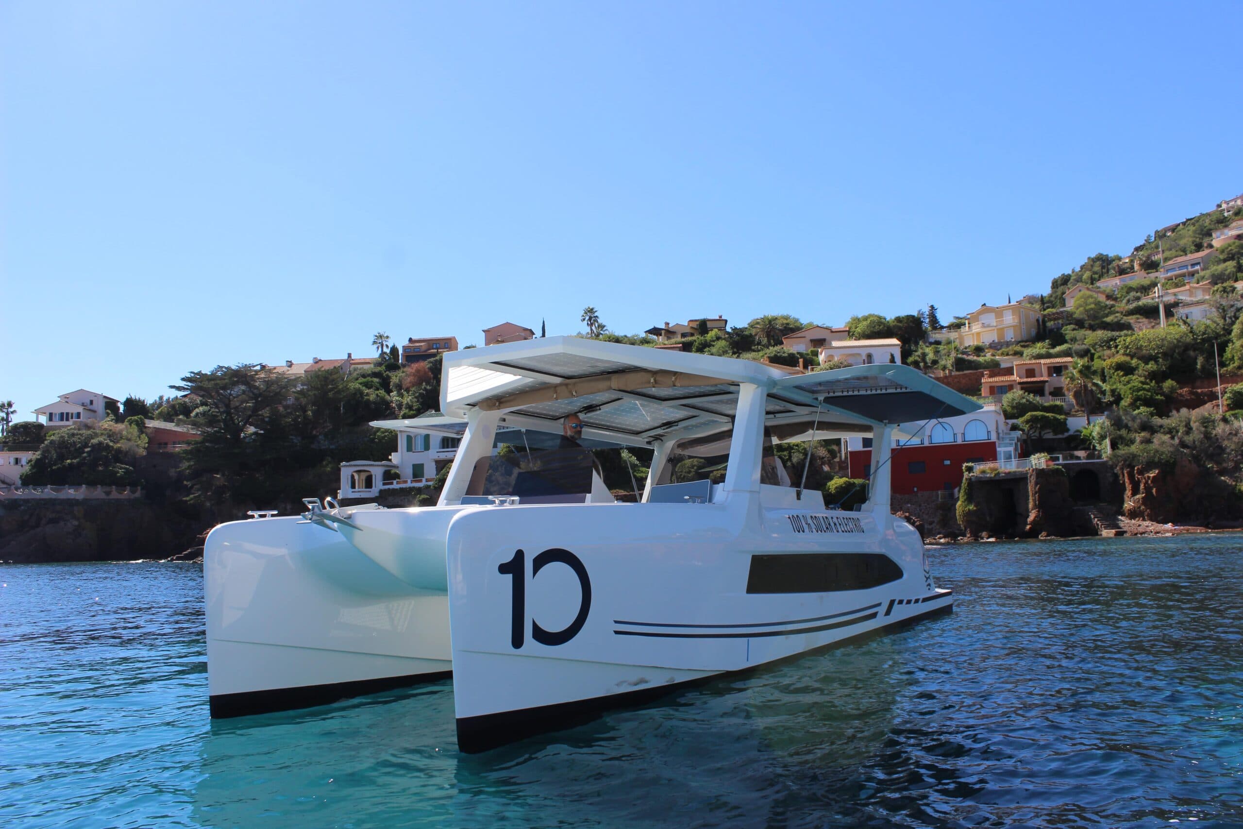 Millikan M10 catamaran viewed from the front-right, showing the bow, hull sides, canopy, and waterline.