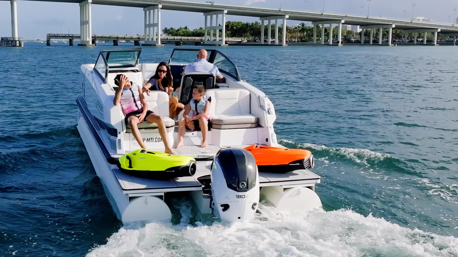 Rear view of a recreational motorboat underway, showing the cockpit, swim platform, outboard motor, and two personal watercraft (2026 Vision Marine SPECTR).