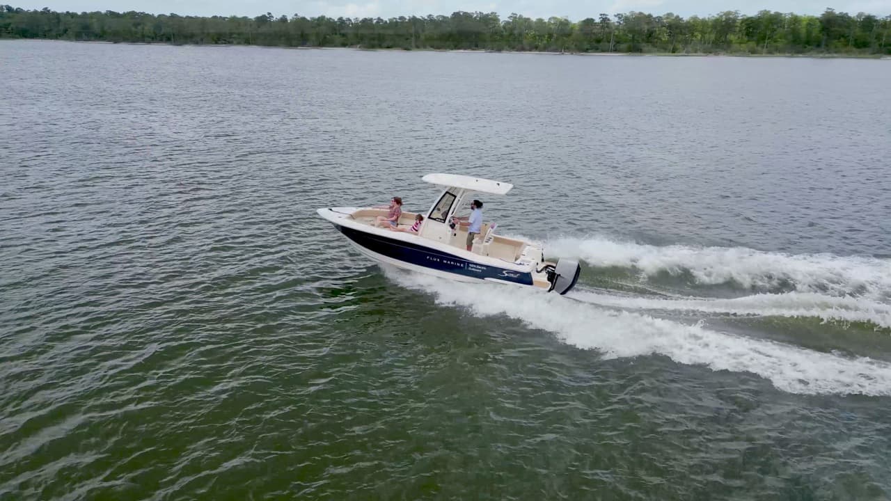 Scout 215 XSF center-console boat viewed from above and to the side, cruising across a lake with its outboard motor underway.