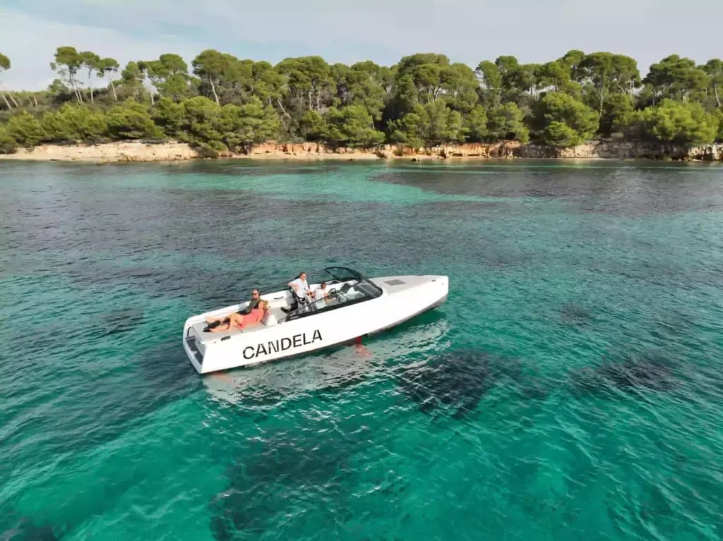 Candela C-8 cruising on turquoise coastal water, viewed from above with a tree-lined shore in the background