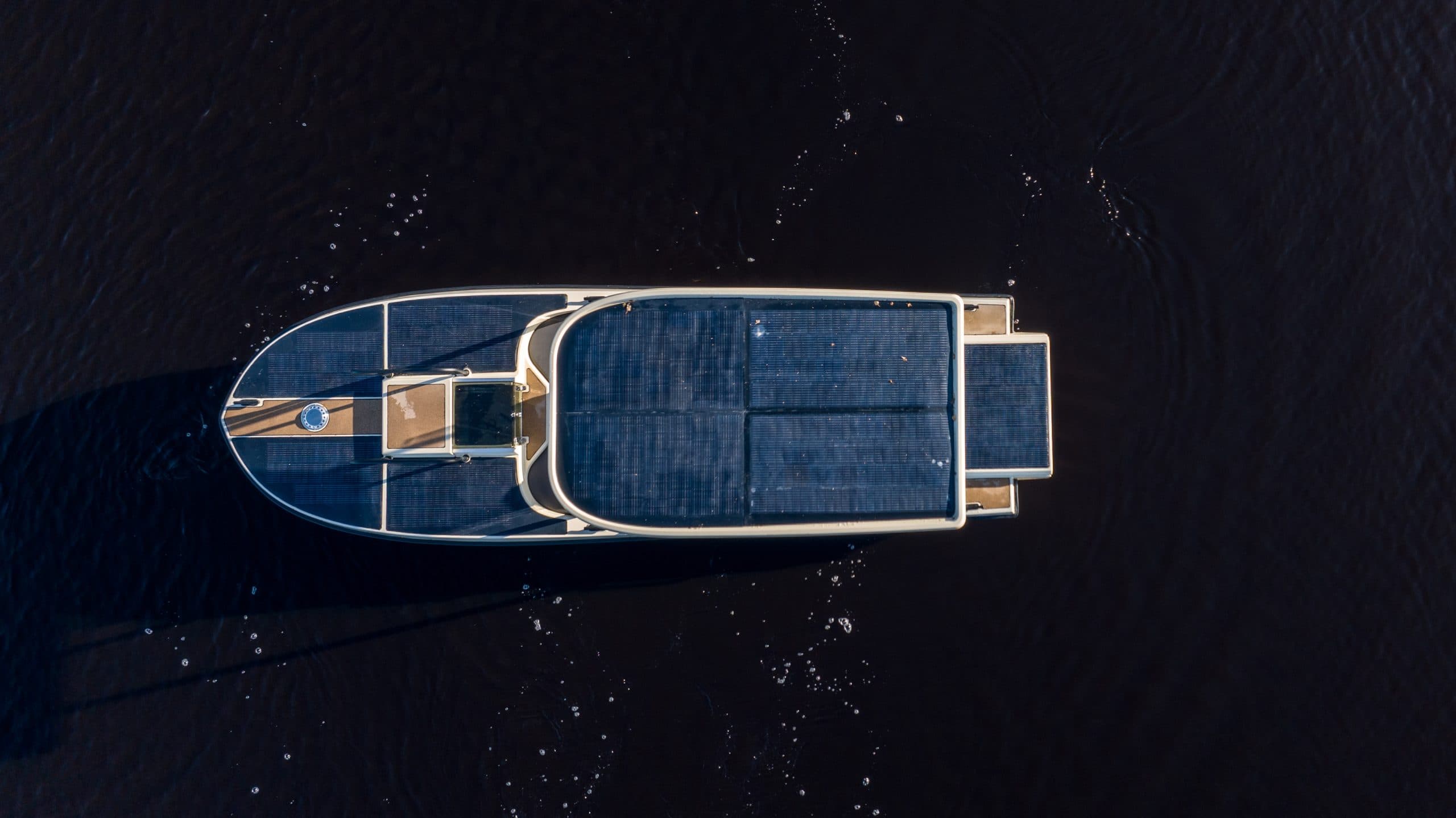 Top-down view of Elvene Amber electric boat idling on dark water, with solar panels covering the deck and the T-top roof