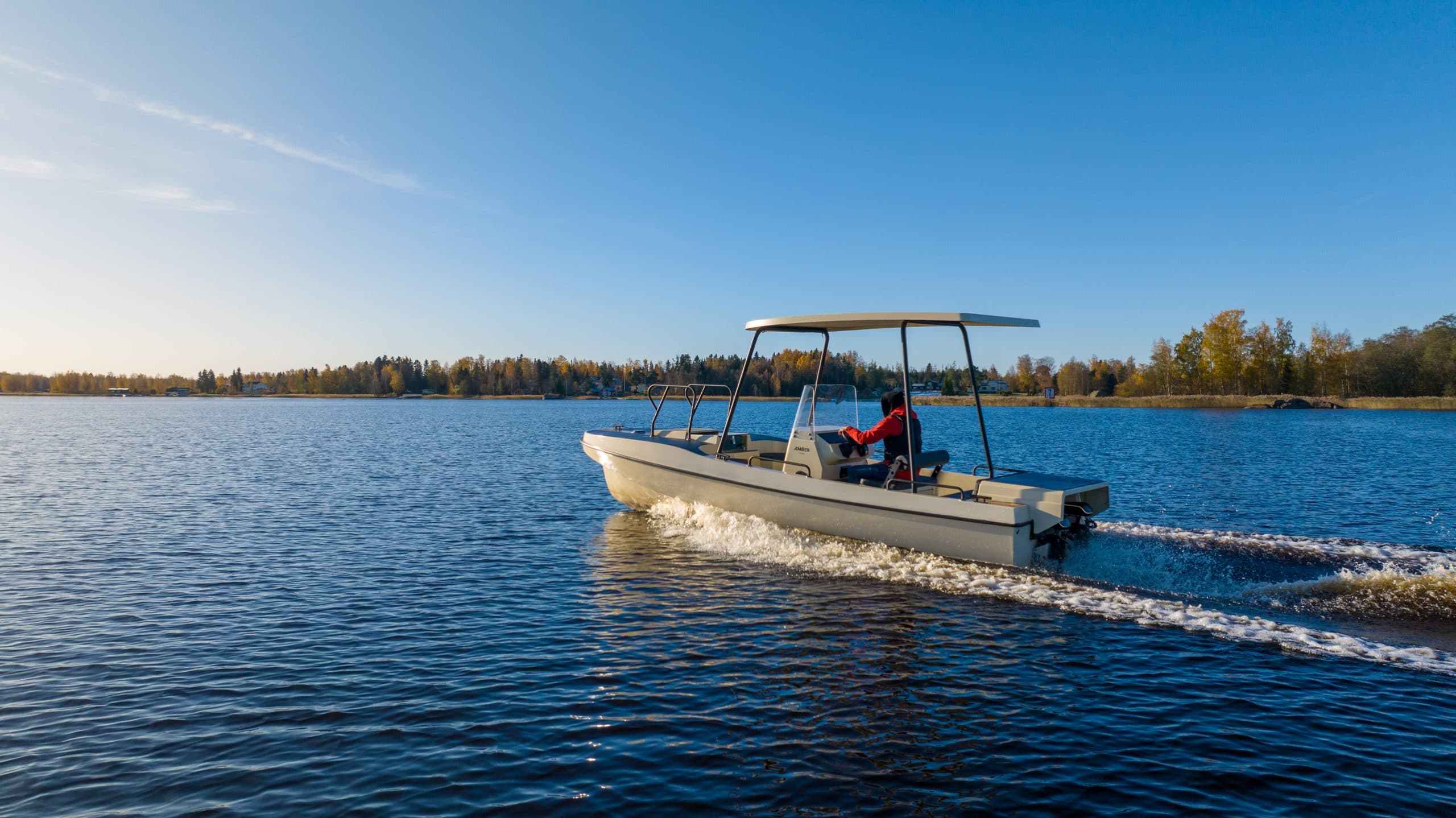 Elvene Amber boat cruising on a lake, with a canopy, two people on board, and a wooded shoreline in the background