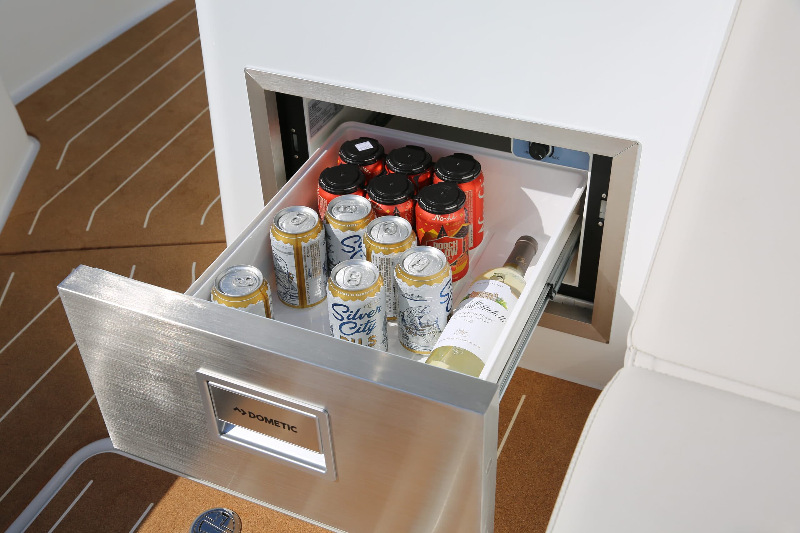 Open marine galley refrigerator drawer stocked with canned and bottled drinks, viewed from above.