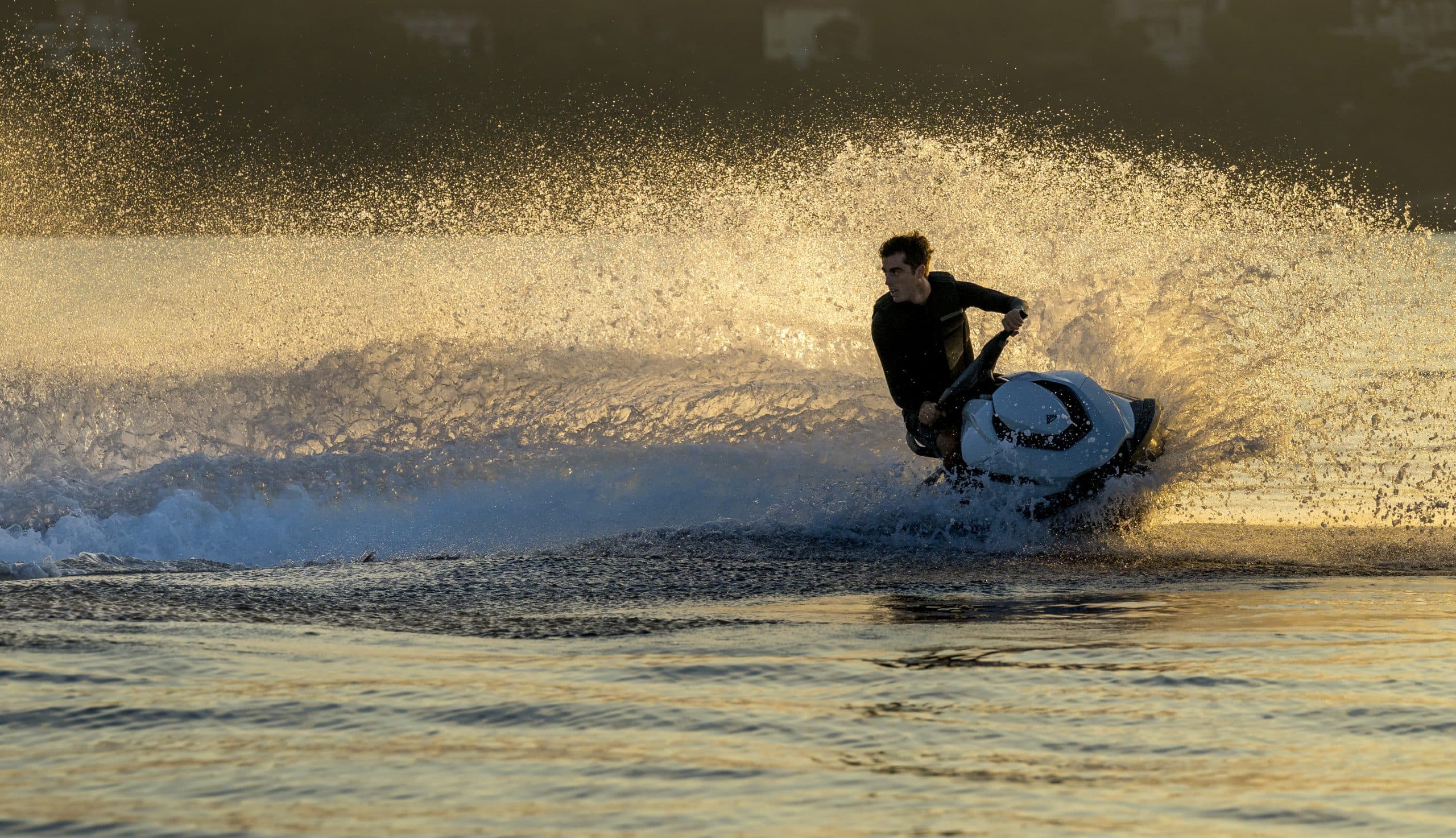 Taiga Orca P2 personal watercraft turning across sunlit water, viewed from the side with spray surrounding the rider.