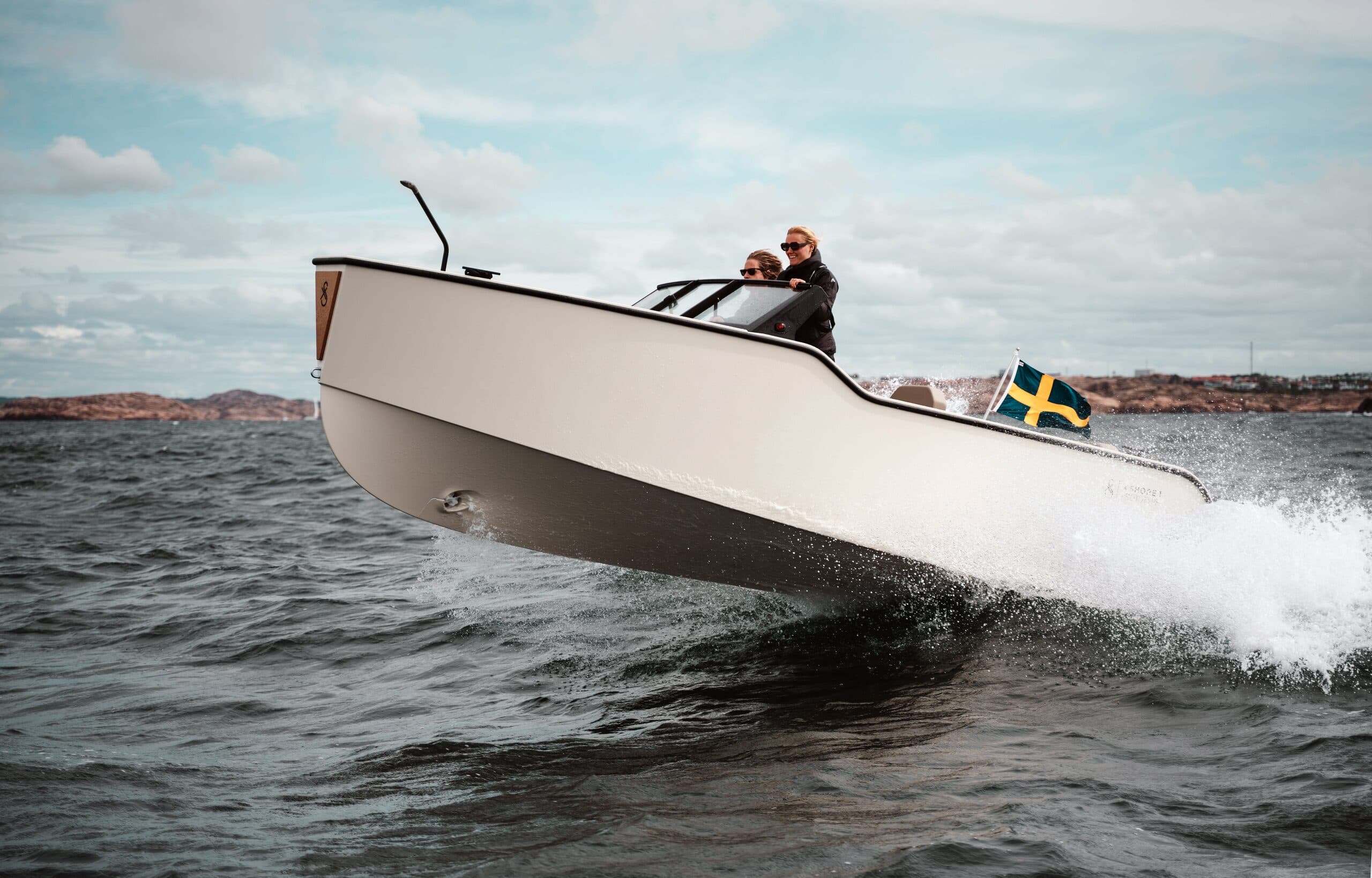 X Shore XS1 speedboat viewed from the side, bow raised as it cuts through choppy water, with a Swedish flag at the stern.